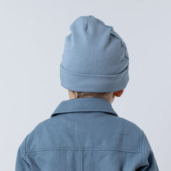 Back view of boy wearing jersey rib beanie hat with rolled hem band in blue