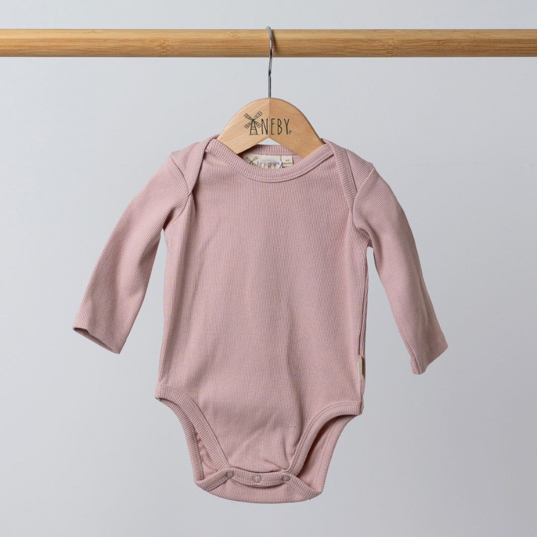 Pink long-sleeved bodysuit hanging from wooden hanger featuring the Aneby logo