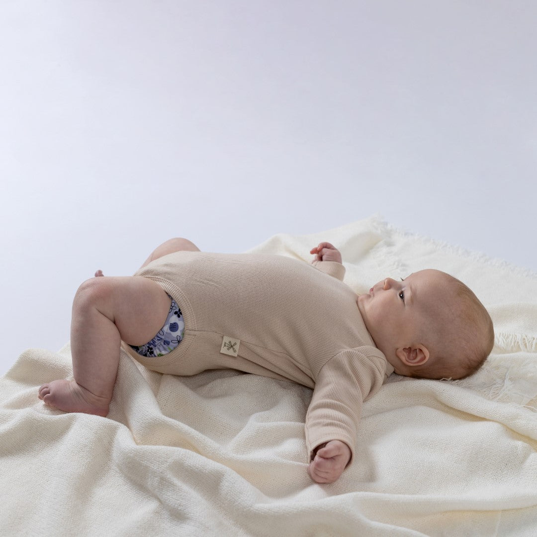 Small baby laying on their back, wearing long-sleeved body suit with Aneby hem tag in focus