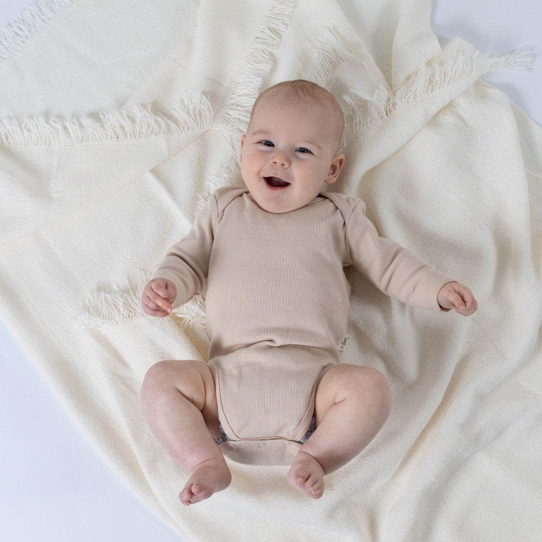 Small baby laughing, wearing cream long-sleeved body suit