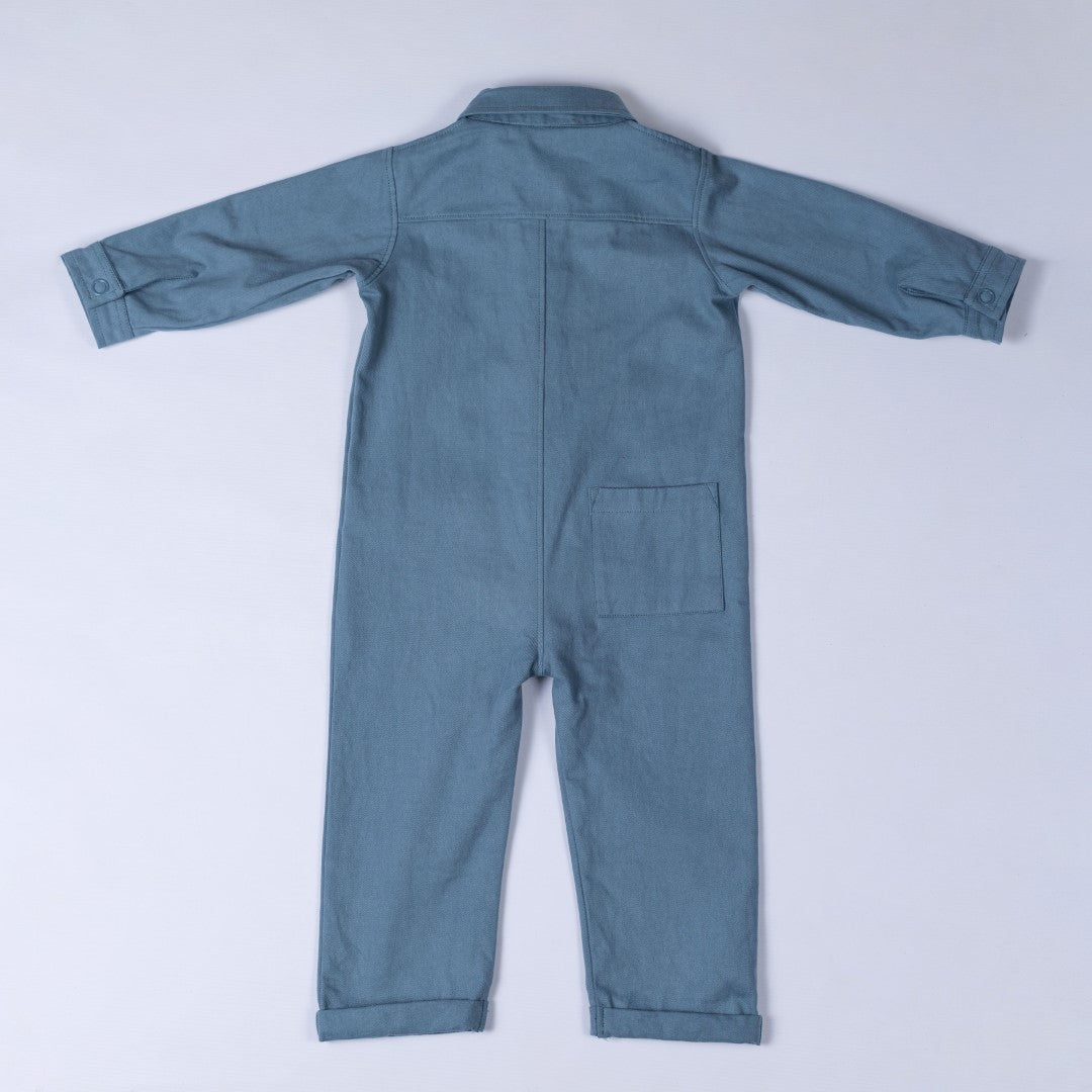 Rear view of the slate blue cotton denim boilersuit with Aneby hem tag