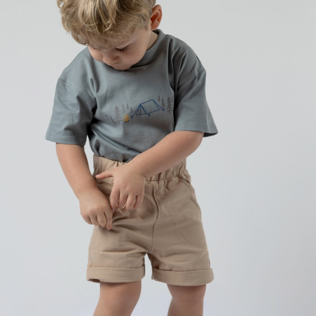 Young model wearing grey camping t-shirt, tucked into stylish beige Aneby shorts