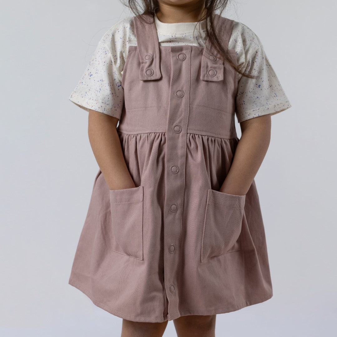 Close up of a model wearing the pastel speckled tee underneath the pink dungaree dress from Aneby