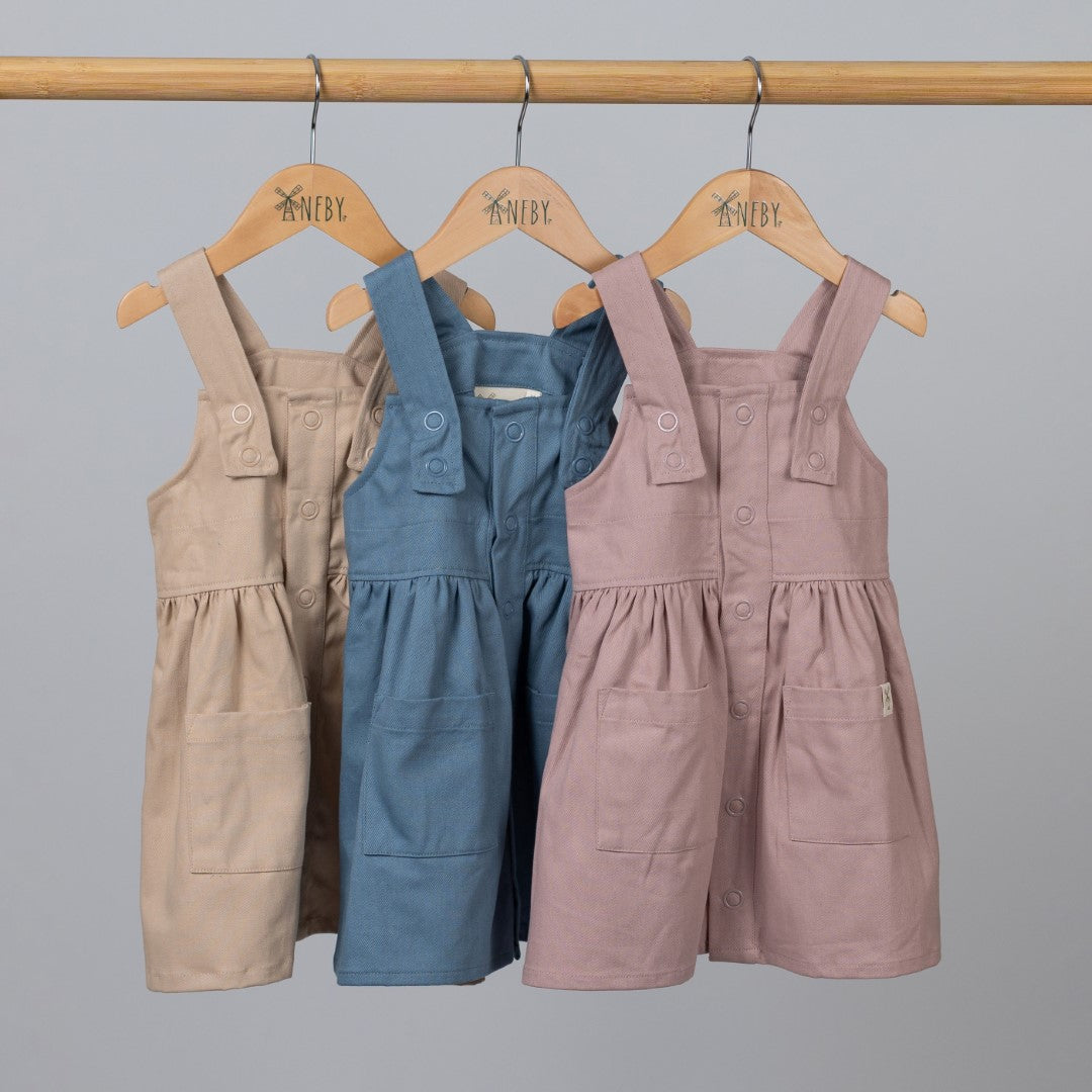 Front view of pleated dresses in beige, blue and pink with front pockets and hem tags