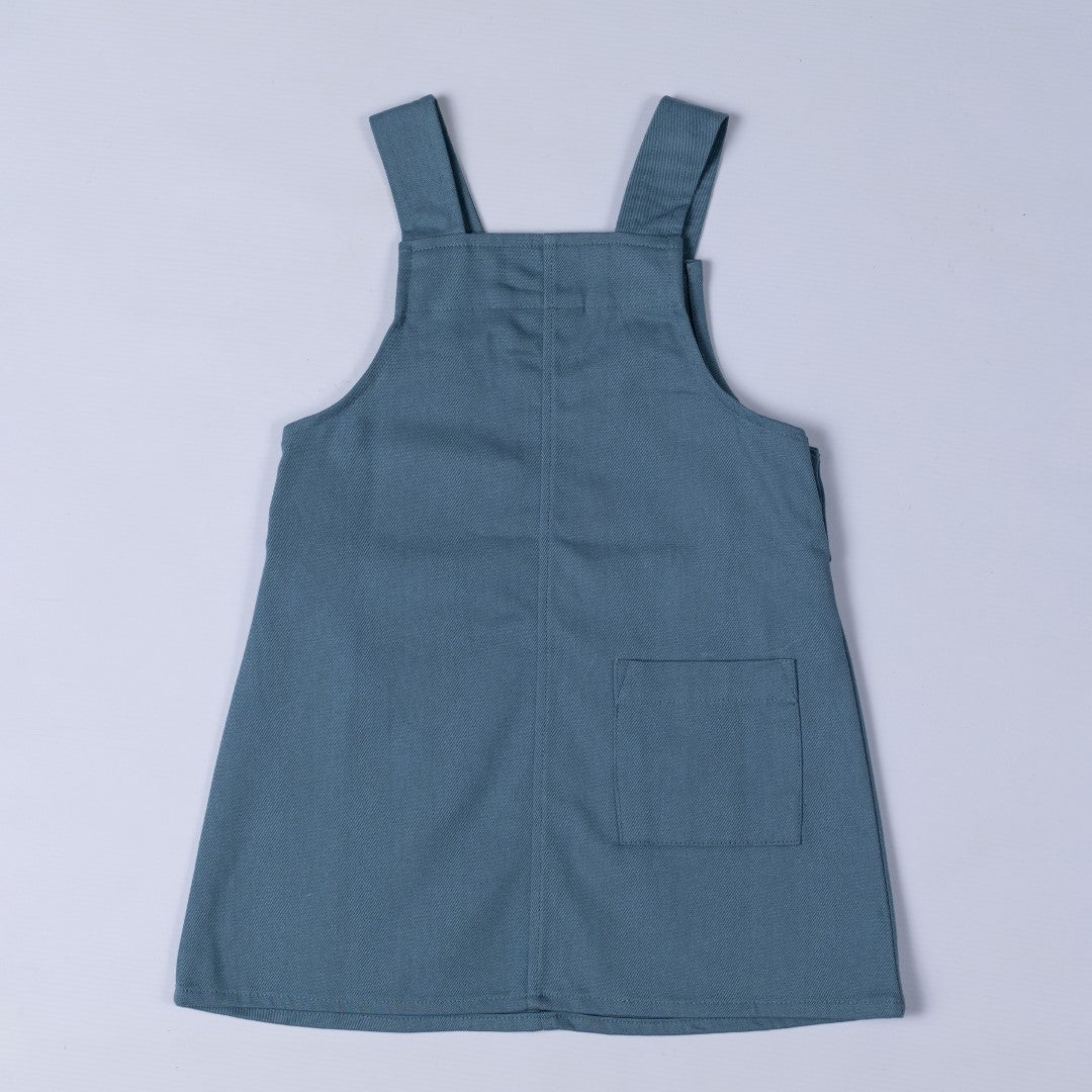 Rear view of slate blue dungaree dress with patch pocket and centre back seam