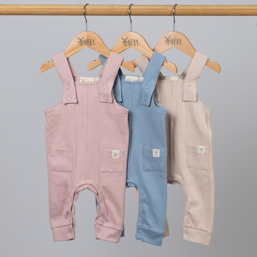 3 pairs of jersey rib dungarees in pink, blue and ecru on Aneby wooden hangers hanging on a wooden clothes rail