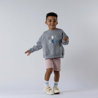 Model blowing bubbles whilst wearing grey sweatshirt with crescent moon design