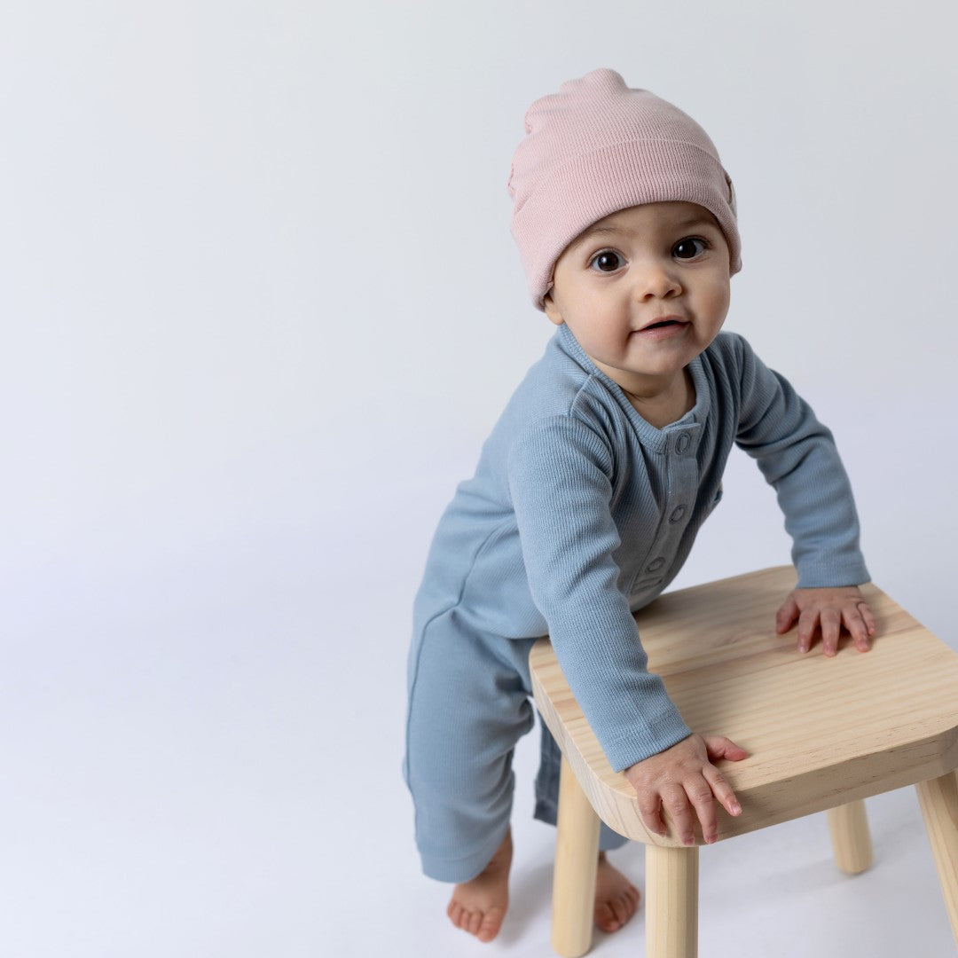 Small baby leaning against wooden stall whilst wearing long sleeved jumpsuit in blue