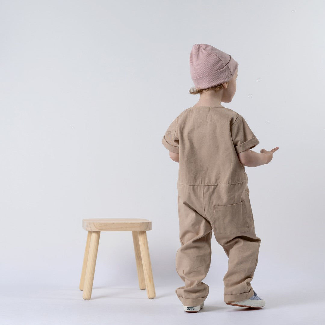 Small girl facing away from the camera with beige jumpsuit and pink beanie