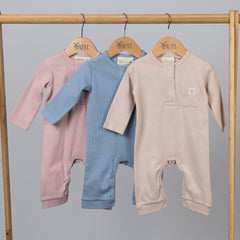 Long sleeved jumpsuits in a range of gender neutral colours hanging from wooden frame