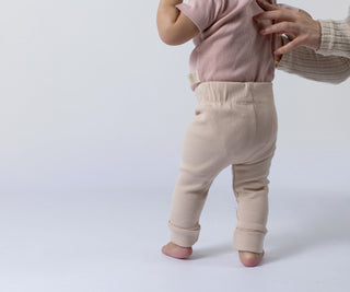 Small baby attempting to stand whilst modelling the beige Aneby leggings