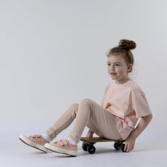 Girl sitting on skateboard looking to the side wearing beige leggings with rolled cuff and pink Aneby Tshirt