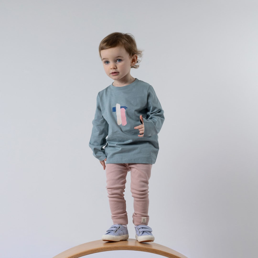 Small Toddler Standing on wooden wobble board wearing pink rib leggings and long sleeve blue tshirt