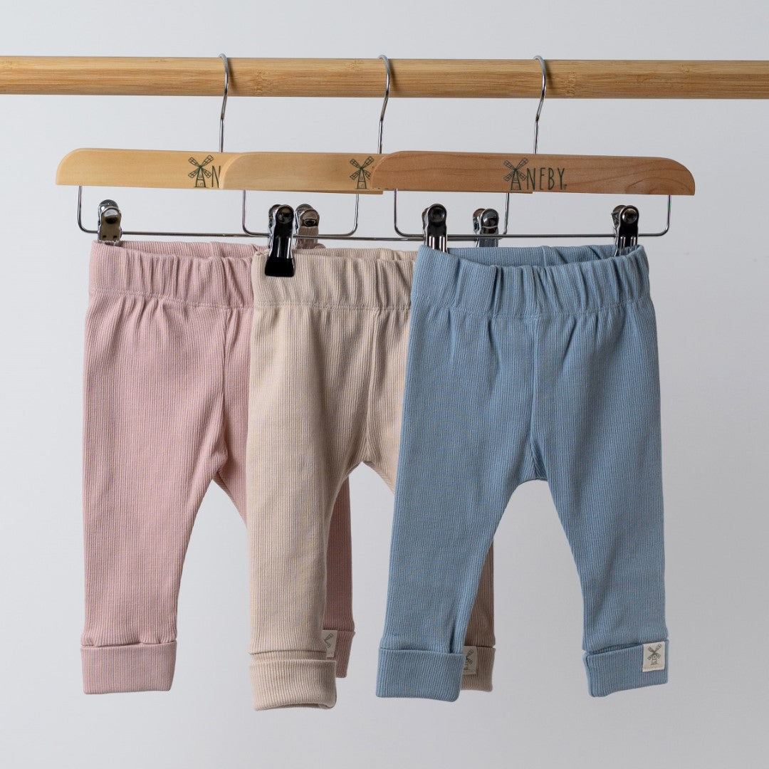 3 pairs of baby leggings in pink, beige and blue on hangers on wooden rail