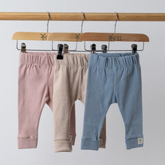 3 pairs of baby leggings in pink, beige and blue on hangers on wooden rail