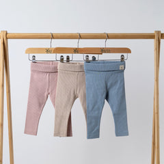 3 pairs of Aneby baby leggings in pink, beige and blue with folded waistband hanging on wooden rail