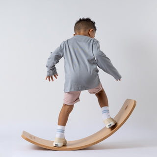 Young model standing on a wooden wobble board sporting a long-sleeve tee and pink shorts