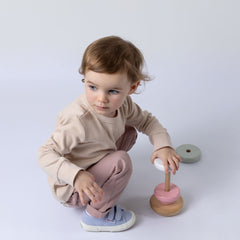 Girl playing with wooden stacking toy wearing long sleeve jersey rib top in oat and blush pink chino trousers