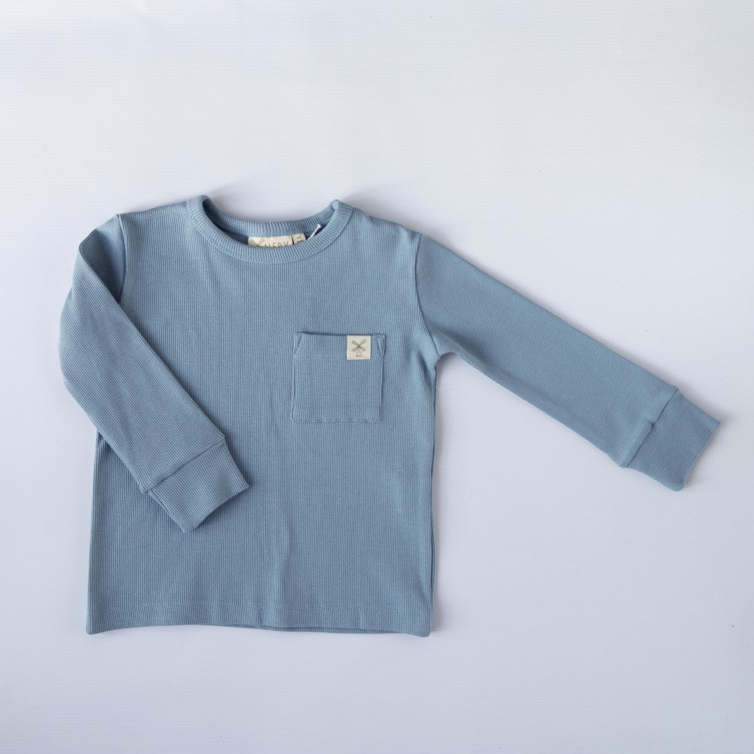 Neutral blue long sleeve top with cuffs and square chest patch pocket with Aneby windmill hem tag