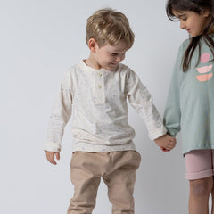 Young boy wearing white long-sleeved t-shirt with speckled effect, holding hands with a small girl