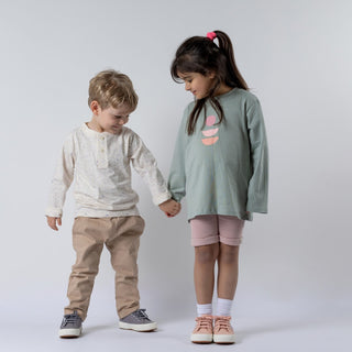 Young girl wearing green long-sleeved t-shirt with abstract print on the front, holding hands with a smaller boy