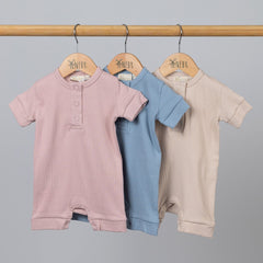 Three playsuits in pink, blue and beige hanging from wooden frame