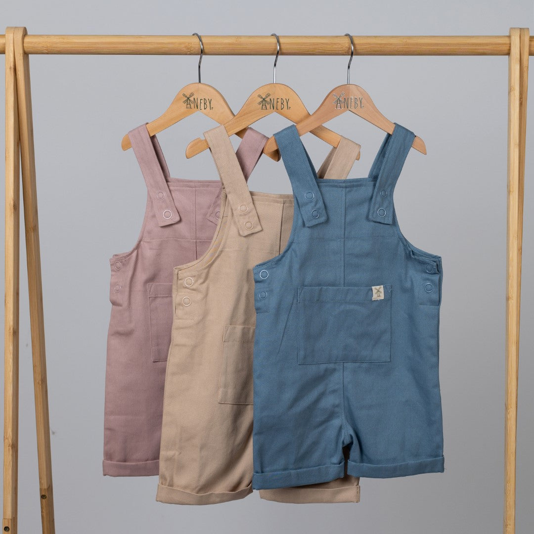 Dungaree shorts in a range on neutral colours hanging from Aneby coat hanger