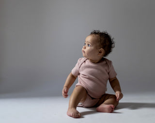 Baby sat down on the floor wearing pink rib short sleeve bodysuit