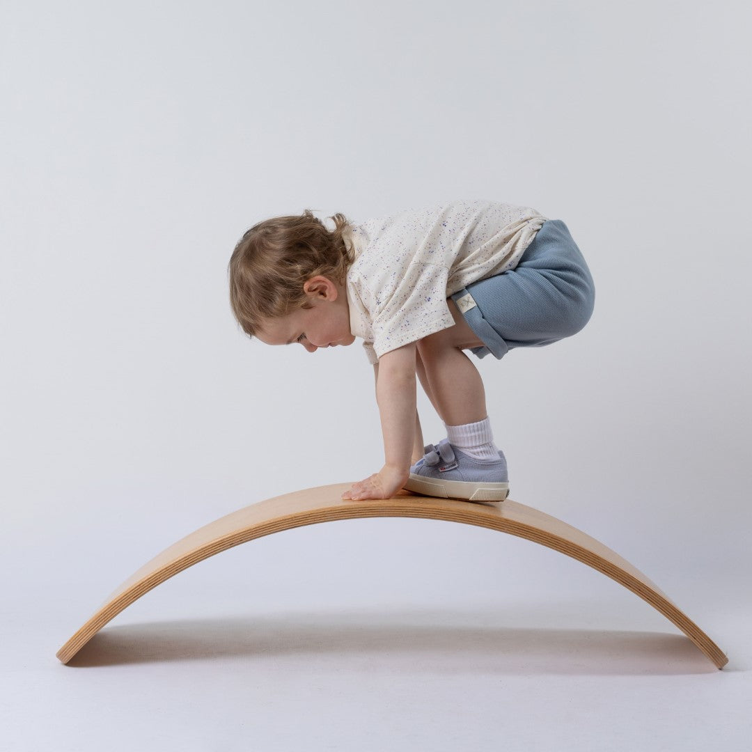 Small child getting her balance on a wooden wobble board whilst modelling the pastel speckled tee from Aneby