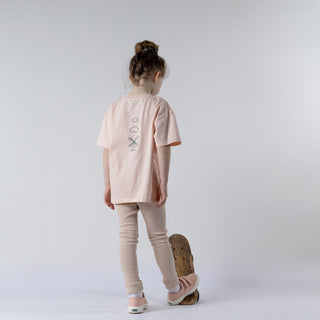 Young girl facing away from camera, wearing a pink t-shirt featuring the Aneby windmill logo and 2 clouds