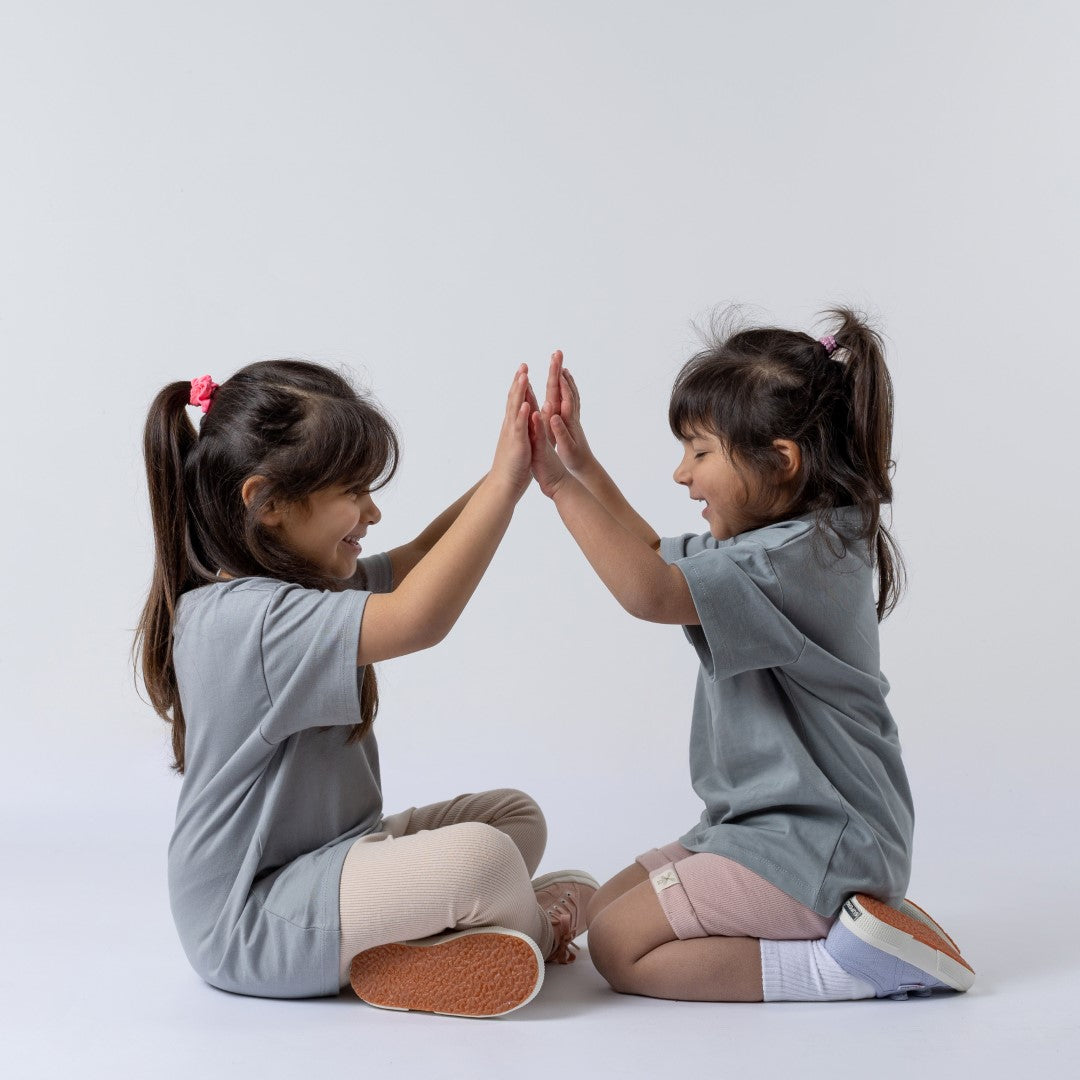 Two girls high-fiving whilst wearing the camping design tee in grey-blue