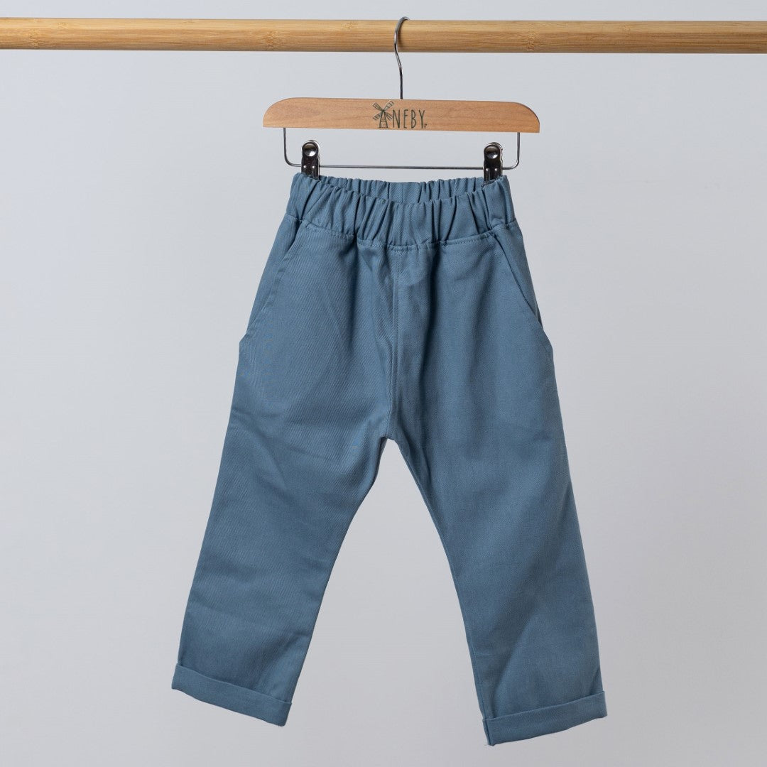 Slate blue trousers with elasticated waist hanging from wooden clothes hanger