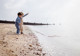 Two Aneby models standing on beach throwing pebbles into the sea