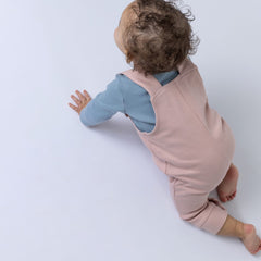 A baby crawling, wearing ribbed cotton dungarees in dusty pink, viewed from the back. The photo emphasises the ribbed detailing and comfortable fit, presented on a simple backdrop.