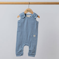 Slate blue sleeveless rib baby romper hanging on a wooden frame, front view. Neutral background.