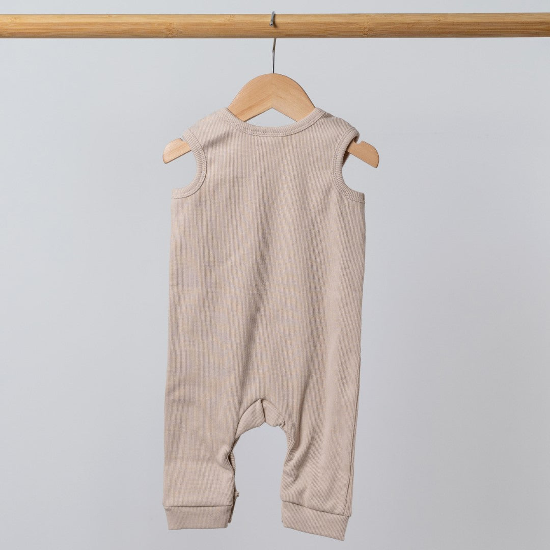 Oat-coloured sleeveless rib baby romper hanging on a wooden frame, back view. Neutral background.