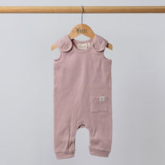 Dusty pink sleeveless rib baby romper hanging on a wooden frame, front view. Neutral background.