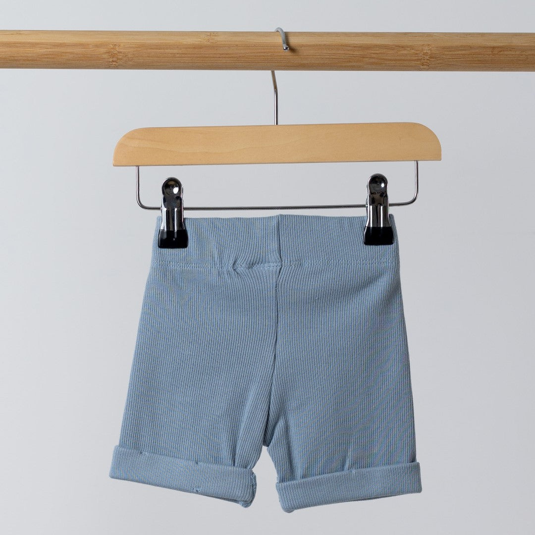 Back view of blue ribbed organic cotton kids shorts hanging on a wooden hanger, with neutral background.