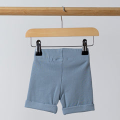 Back view of blue ribbed organic cotton kids shorts hanging on a wooden hanger, with neutral background.
