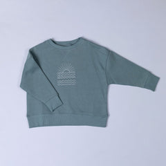 Flat lay of a steel blue sweatshirt featuring a white sunrise graphic on the front, displayed against a neutral background.