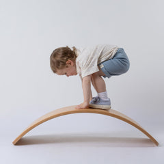 Small girl leaning over on a wobble board, wearing slate blue ribbed organic shorts with ecru t-shirt, set against a neutral background.