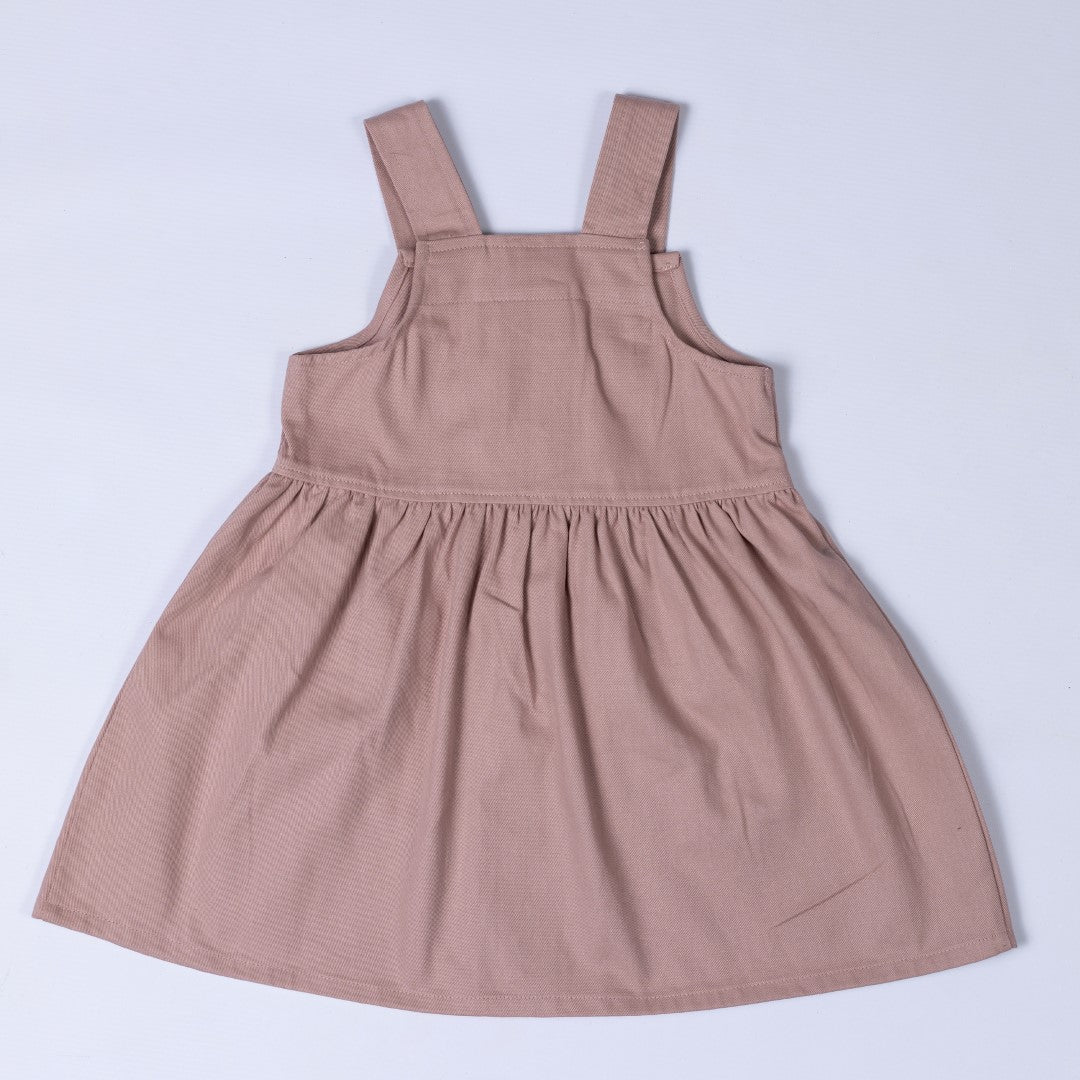 Flat lay of the back of a dusty pink girls’ pleated dress with straps, displaying the pleated skirt and back strap construction.