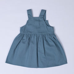 Flat lay of the back of a slate blue girls’ pleated dress with straps, focusing on the pleats and back strap details.