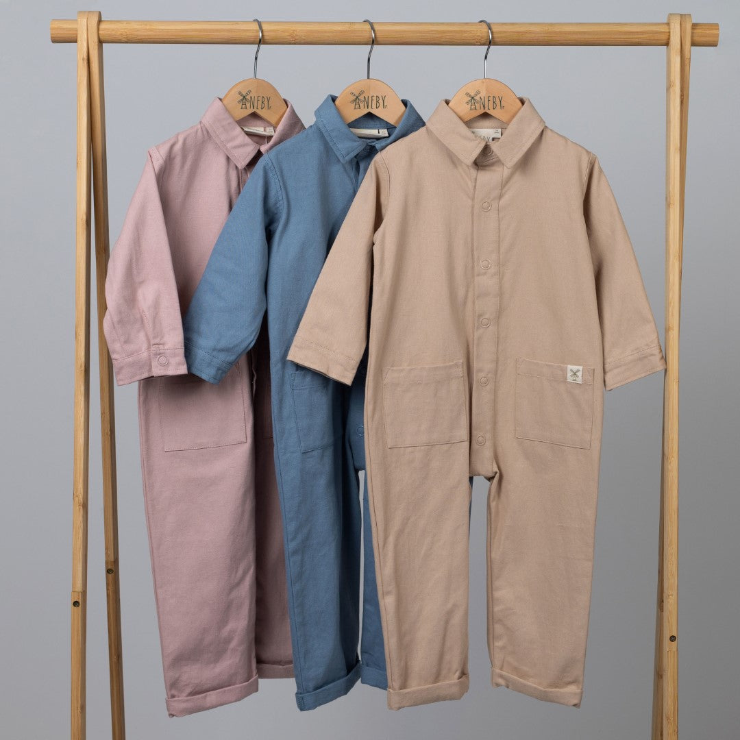 Set of three children's boilersuits in oat, slate blue, and dusty pink, displayed together.