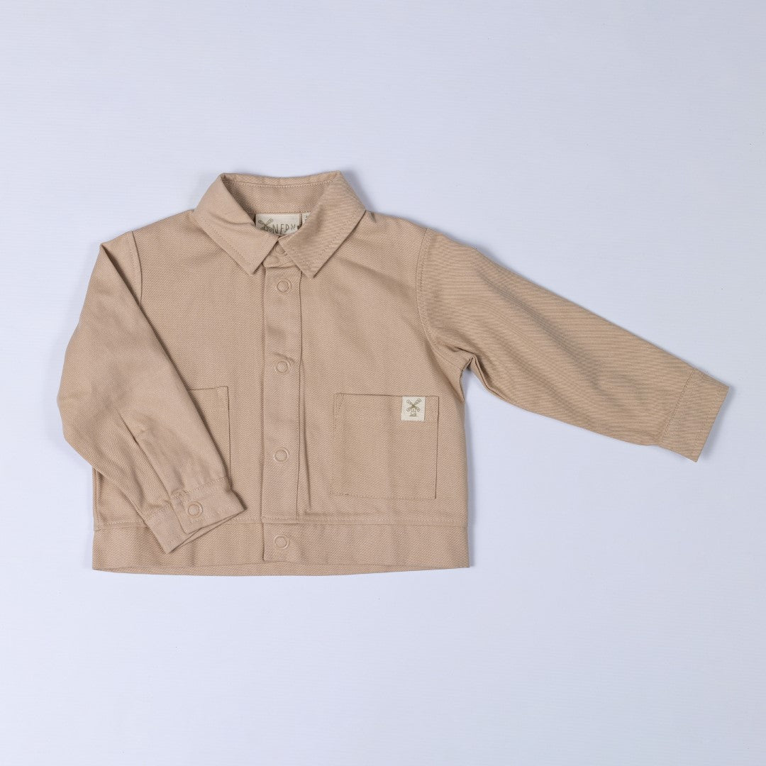 Front view of an oat-coloured kids' organic cotton shacket with a soft twill finish and front popper closure.