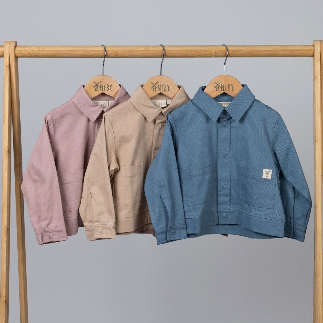 A set of three kids' organic cotton shackets in slate blue, dusty pink, and oat, displayed together.