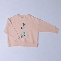 Flat lay of a kids pink sweatshirt featuring a unique design of vertical moons, horseshoes, and small suns in blue and green tones.