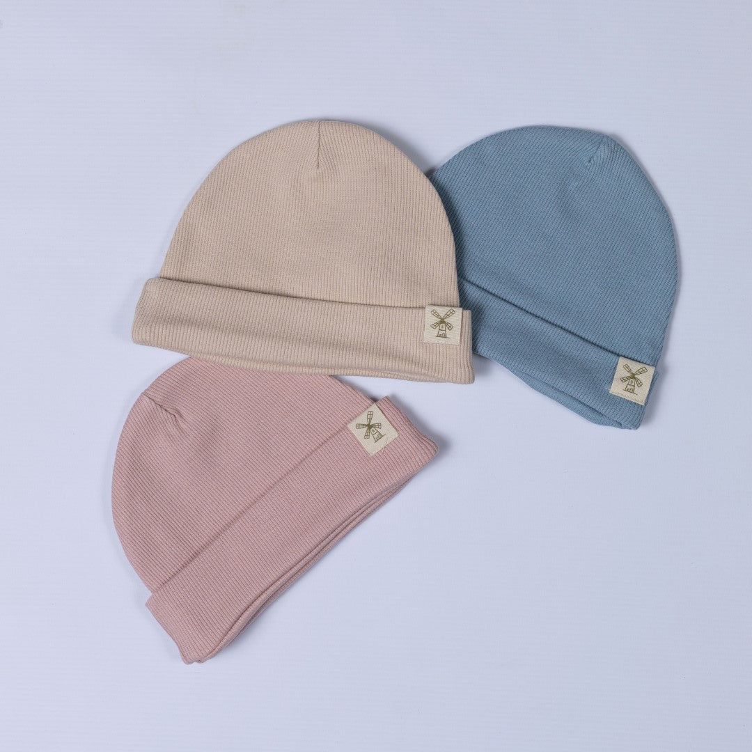 Three kids ribbed cotton beanie hats in blush pink, slate blue, and oat, made from soft organic cotton.