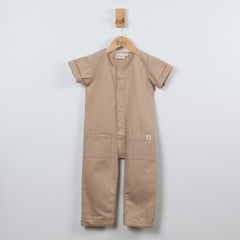 Beige short sleeve overall hanging on a wooden hanger with a front view in a neutral background.