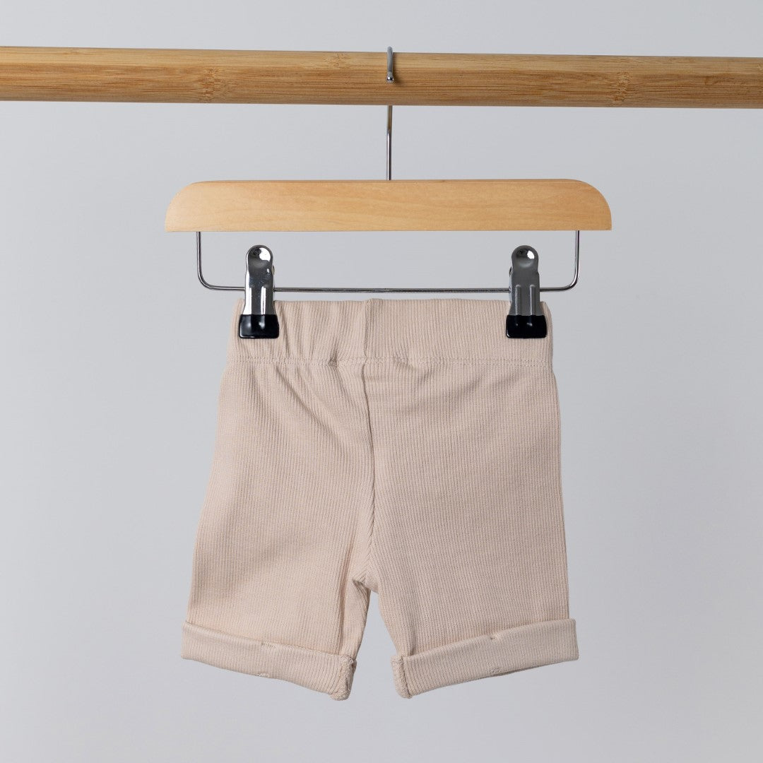 Back view of oat ribbed organic cotton kids shorts hanging on a wooden hanger, with neutral background.